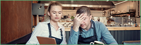 Coface Focus - the business insolvency paradox in Europe: miracle and mirage. The photo shows a man and a woman in a café worried about their corporate finances.
